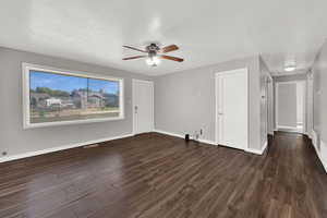 Unfurnished living room featuring a ceiling fan, dark wood-style flooring, and a textured ceiling