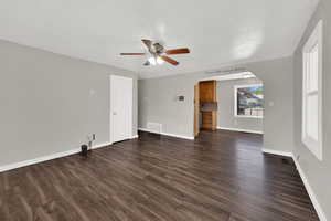 Unfurnished living room with ceiling fan, arched walkways, and dark wood-type flooring