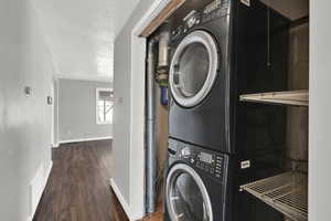 Laundry room with stacked washer and clothes dryer, wood finished floors, and a textured ceiling