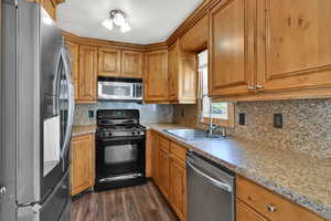 Kitchen featuring appliances with stainless steel finishes, backsplash, dark wood-style flooring, and brown cabinetry
