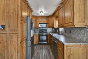 Kitchen with stainless steel appliances, brown cabinets, dark wood-style flooring, and decorative backsplash