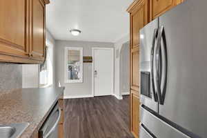 Kitchen with stainless steel appliances, dark wood finished floors, brown cabinetry, and decorative backsplash