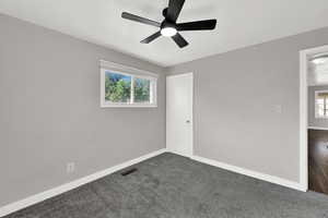 Empty room featuring a ceiling fan and dark colored carpet