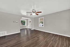 Unfurnished living room with ceiling fan, dark wood finished floors, and arched walkways