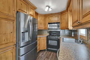 Kitchen featuring stainless steel appliances, dark wood-style floors, tasteful backsplash, and brown cabinetry