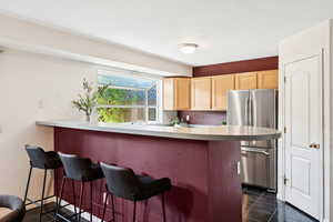 Kitchen featuring light brown cabinets, freestanding refrigerator, a kitchen bar, dark tile patterned floors, and a peninsula