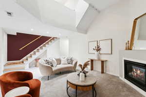 Living area with carpet flooring, stairs, high vaulted ceiling, and a glass covered fireplace