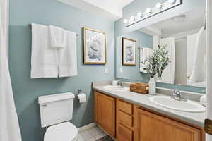 Full bathroom with double vanity, tile patterned floors, and curtained shower