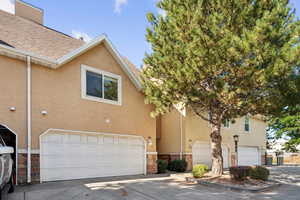 View of front of home featuring a garage, concrete driveway, stone siding, and stucco siding