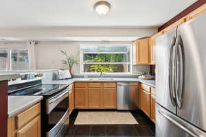 Kitchen featuring appliances with stainless steel finishes, plenty of natural light, dark tile patterned flooring, light countertops, and a textured ceiling