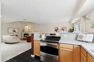 Kitchen featuring stainless steel electric range, dark colored carpet, open floor plan, and light countertops