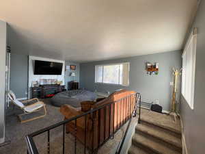 Living area with a textured ceiling, carpet, a baseboard radiator, and stairs