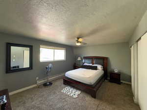 Carpeted bedroom with a textured ceiling, a baseboard heating unit, and ceiling fan
