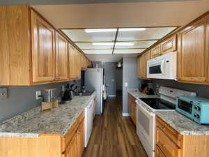 Kitchen featuring white appliances, dark wood finished floors, and light stone countertops