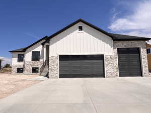View of front of home featuring a garage, concrete driveway, stone siding, and board and batten siding