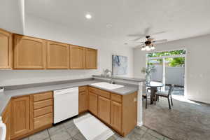 Kitchen with a peninsula, white dishwasher, a ceiling fan, light countertops, and light colored carpet