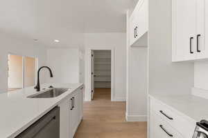 Kitchen with white cabinets, light wood-style flooring, dishwasher, light stone countertops, and recessed lighting
