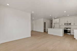 Kitchen featuring white cabinets, open floor plan, stainless steel appliances, light countertops, and recessed lighting