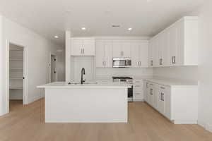 Kitchen featuring stainless steel appliances, white cabinets, light wood-type flooring, a kitchen island with sink, and recessed lighting
