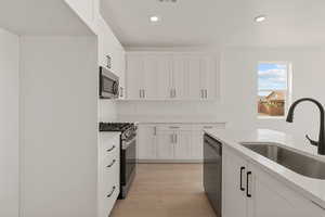 Kitchen with appliances with stainless steel finishes, white cabinetry, light stone countertops, recessed lighting, and light wood-style flooring