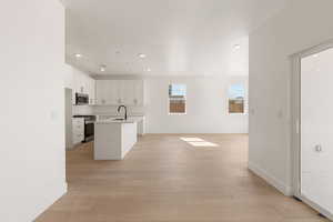 Kitchen with white cabinetry, appliances with stainless steel finishes, an island with sink, light wood-type flooring, and recessed lighting