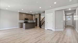 Kitchen featuring open floor plan, a textured ceiling, light wood finished floors, an island with sink, and recessed lighting