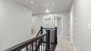 Hallway featuring an upstairs landing and light colored carpet