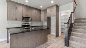 Kitchen with a textured ceiling, stainless steel appliances, light wood-type flooring, dark stone countertops, and an island with sink