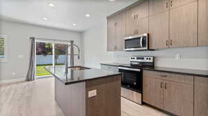 Kitchen featuring stainless steel appliances, a textured ceiling, light wood-style floors, an island with sink, and recessed lighting
