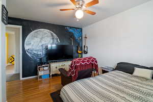 Bedroom with wood finished floors, an accent wall, and a ceiling fan