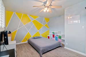 Bedroom with an accent wall, wood finished floors, wallpapered walls, and a ceiling fan
