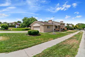 View of home's exterior featuring a garage, a chimney, a lawn, brick siding, and driveway
