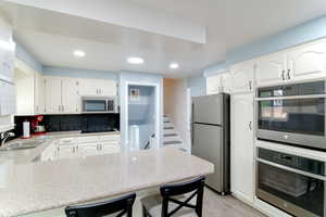 Kitchen with stainless steel appliances, a peninsula, backsplash, a kitchen breakfast bar, and white cabinetry