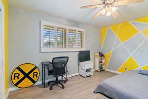 Bedroom featuring wood finished floors, a ceiling fan, and an accent wall