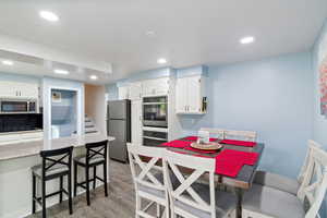 Kitchen with white cabinetry, light wood finished floors, stainless steel appliances, recessed lighting, and a breakfast bar