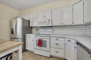 Kitchen featuring appliances with stainless steel finishes, white cabinets, light countertops, and decorative backsplash
