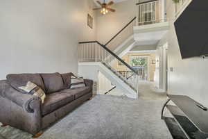 Carpeted living area with a high ceiling, ceiling fan, and stairs