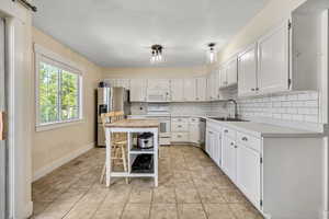 Kitchen with backsplash, appliances with stainless steel finishes, white cabinets, and light tile patterned floors