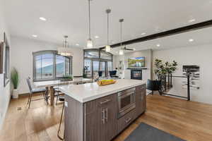 Kitchen featuring beamed ceiling, a center island, recessed lighting, light wood-style flooring, and a glass covered fireplace