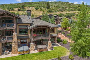 Rear view of property featuring a hot tub, a balcony, a patio area, stone siding, and a chimney