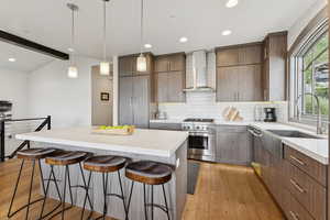 Kitchen featuring light wood-style floors, stainless steel appliances, a breakfast bar area, wall chimney range hood, and beamed ceiling