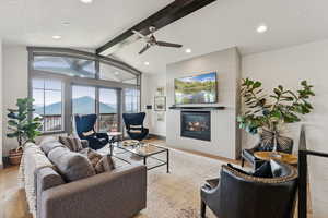 Living area with beam ceiling, a tile fireplace, wood finished floors, ceiling fan, and recessed lighting
