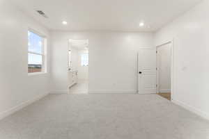 Unfurnished bedroom with light carpet, ensuite bathroom, and recessed lighting