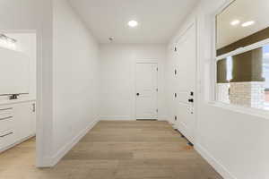 Hall with light wood finished floors and recessed lighting