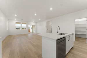 Kitchen with white cabinets, a center island with sink, light wood finished floors, open floor plan, and stainless steel dishwasher
