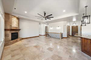 Unfurnished living room with ceiling fan, a tiled fireplace, recessed lighting, a tray ceiling, and light stone finish floors