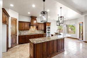 Kitchen with decorative backsplash, a large island, recessed lighting, premium range hood, and light stone counters