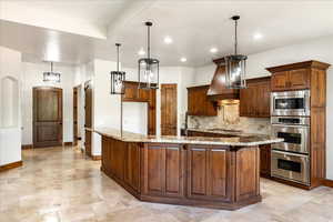 Kitchen featuring appliances with stainless steel finishes, a spacious island, light stone counters, recessed lighting, and custom exhaust hood