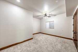 Carpeted spare room with a ceiling fan and baseboards