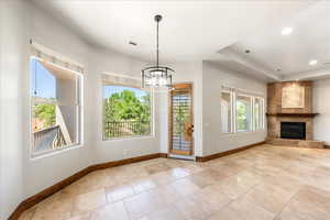 Unfurnished dining area with a chandelier, a tiled fireplace, a raised ceiling, and recessed lighting